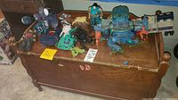 Photo showing wooden toy chest with multiple Transformer figures on top in various colors and forms, including vehicle and robot modes.