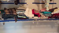 Full view of folded children's clothes on a white shelf showing different types of clothing including denim jeans, sweaters, and vests in assorted colors and patterns.