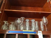 Wide view of all glassware items in wooden cabinet shelf showing arrangement of Irish coffee glasses, wine glasses and pilsners