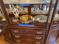 Various serveware displayed on cabinet shelves including metal chargers, cut glass decanters, square plates.