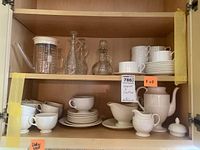 Shelf with Fitz and Floyd cups and saucers, Wedgwood coffee pot, cream pitcher, gravy boat, plates, and glass cruets.