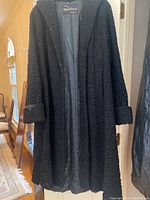 Front view of the black full-length mouton lamb fur coat hanging on a door, showing fur texture and satin lining inside.