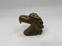 Front angle view of carved stone eagle's head showing detailed beak and feather carving on neutral background.