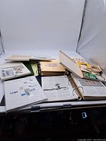 Photo of stamp albums and binders laid open with stamps displayed on pages, plus loose stamp sheets.