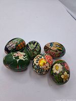 Photo showing all six hand-painted decorative eggs arranged on a surface, illustrating varied designs including flowers, animals, and a rider on horseback.