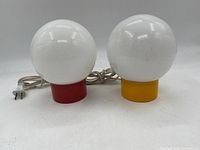 Pair of two vintage 1970s bulb table lamps with white glass globe shades and colored cylindrical bases in red and yellow, including attached electrical cords and plugs.