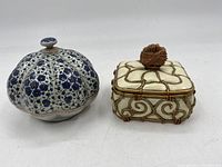 Pair of small trinket dishes shown side by side, one rounded with floral pattern, the other square with cream lacquer and wire details