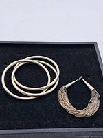Full view of the two bracelets on black background, showing tri-bangle set and multi-strand wire bracelet