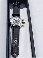 Front view of watch in original box, showing black crocodile-pattern leather strap and stainless steel case