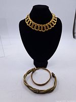 Three vintage necklaces shown on black display; one large link gold-tone choker, twisted multi-strand necklace, and twisted metal collar necklace