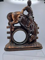 Full view of the bronze-tone metal cowboy riding horse clock frame showing the hollow circular clock section and detailed cowboy figure