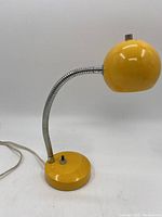 Full view of vintage yellow desk lamp showing the round base with toggle switch, flexible silver gooseneck arm, and spherical yellow shade.