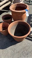 Full view of all four terra-cotta pots varying in size, showing natural reddish clay color and some wear with light chips and cracks.