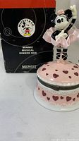 Front angle showing pink heart decorated musical box base with Minnie Mouse figurine standing on top, box in background.