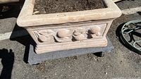 Top and side views of the rectangular concrete planter showing dirt and ornate raised fruit-leaf design on the side panels.