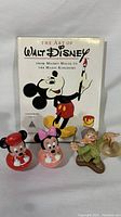 The Art of Walt Disney book with Mickey Mouse cover featuring three Disney character figurines in front: Dopey, Mickey Mouse, and Minnie Mouse roly poly toys.
