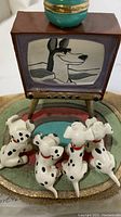 Close-up front view of the five Dalmatian puppies sitting and facing the vintage TV figurine with lamp, showing the TV screen image and puppies' details.