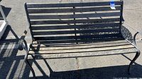Full view of the wood and metal outdoor bench showing slatted wooden seat/back with metal frame and curved armrests.