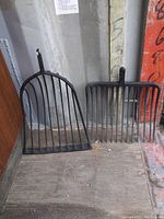 Front view showing both cast iron heads, fork on left and shovel on right, placed on wooden floor against a gray wall.