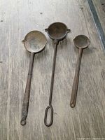 All three antique cast iron ladles laid flat on wooden surface showing size and condition