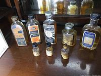 Front view of a collection of vintage glass oil bottles with labels showing various types including machine oil, stainless machine oil, castor oil, and bottles partially filled with contents.