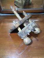 Antique wooden hand plane resting on a wooden surface next to a mirror, showing the turned wood adjustment screws and wooden knobs from above at an angle.