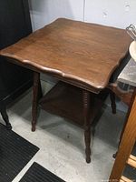 Angle view showing scalloped wood tabletop and turned legs with lower shelf