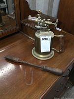 Photo showing both the antique brass gas torch with wood handle and the old soldering iron with copper head on wooden surface.