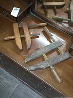 Photo of two antique wooden hand clamps on a wooden surface, showing wood threaded screws and handles with aged wear.