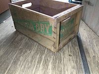 View of the wooden crate showing Canada Dry logo on the longer side with handle cutout on the side panel