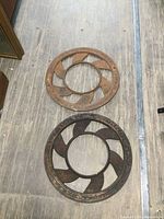Two round cast iron floor grates placed on wooden floor, one rusted orange and the other dark rusty brown.