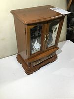 Closed wooden jewelry box with glass etched floral design on doors, brass handles on front and bottom drawer, showing exterior condition.