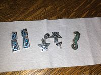 Four silver jewelry pieces displayed on white cloth: two pairs of earrings and one seahorse brooch, showing front and back views.