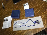 Full lot including pendant necklace, presentation box, tag and certificate leaflet displayed on table