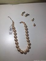 Necklace and two pairs of earrings shown on flat surface with necklace tag visible.