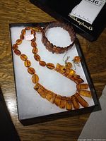 Set of amber style necklace, bracelet, and earrings on white padding with box lid in background.