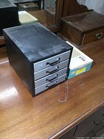 Photo of vintage metal parts cabinet with four drawers sitting on wooden surface.