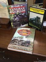 Photo showing the three hardcover railroad books arranged on wooden surface, covers visible with locomotives, including "Railroad Recollections," "50 Years of Canadian Railroads," and "Encyclopedia of Railways."