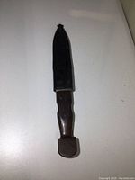 Full view of the vintage cutter with the black sheath on a white surface.