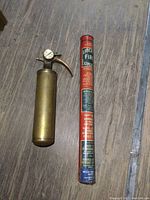 Photo of vintage brass fire extinguisher next to a Liberty single use fire extinguisher on wooden floor