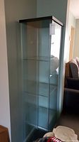 Full view of tall glass door cabinet showing black frame and four clear glass shelves.