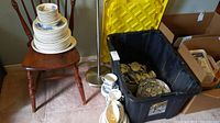 Stack of plates and saucers on a small wooden chair alongside a black storage bin containing various blue and white china pieces