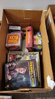 Photo showing several board games in a cardboard box, viewed from above.
