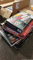 Stack of assorted boxed board games including Mahjong and Gigantik, showing packaging and titles clearly.