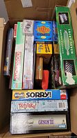 Photo showing a box with multiple board games including Monopoly, Sorry!, Trivial Pursuit Genus III, Wizard card game, Lucky Seven set, Pictionary Quick Sketch, and a wooden chess/checker set.