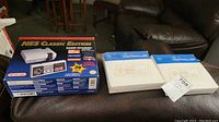 Photo showing NES Classic Edition console box and two ATA brand controllers in box on sofa, unopened.