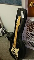 Black Rocker electric guitar leaning against soft carrying case and amplifier, showing full guitar body and neck.