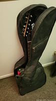 Partial view of the black padded guitar soft case with guitar inside, partially unzipped.