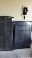 Two large dog kennel black plastic bases embossed with 'DURALAST ENGLAND MADE Y1482' leaning against a wall along with metal kennel frames.