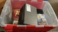 Plastic storage bin containing DVDs and black leather DVD case with stitched edges, partially opened revealing DVD sleeves inside.